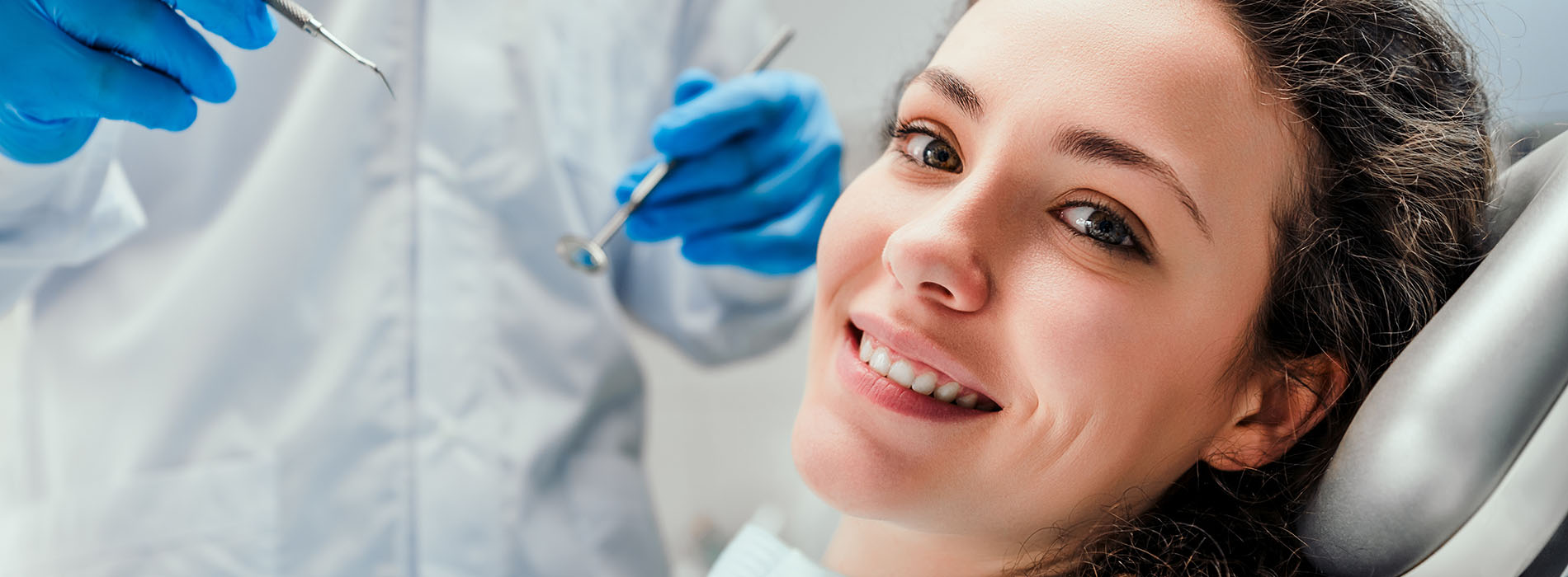 The image shows a person receiving dental care, with a dental hygienist or dentist performing an oral examination using a mirror and dental instruments.