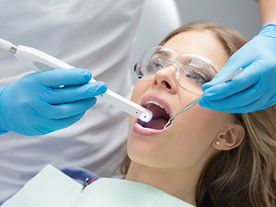 The image shows a dental professional performing oral care on a patient using a dental device, with the patient seated in a chair and wearing a surgical mask.